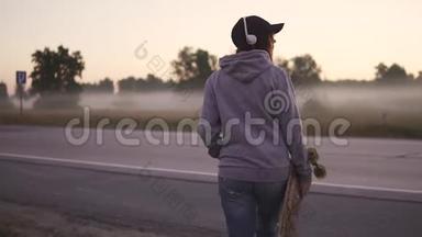 一个手拿滑板的时髦女孩的特写肖像。 那个红发女孩沿着废弃的公路走着